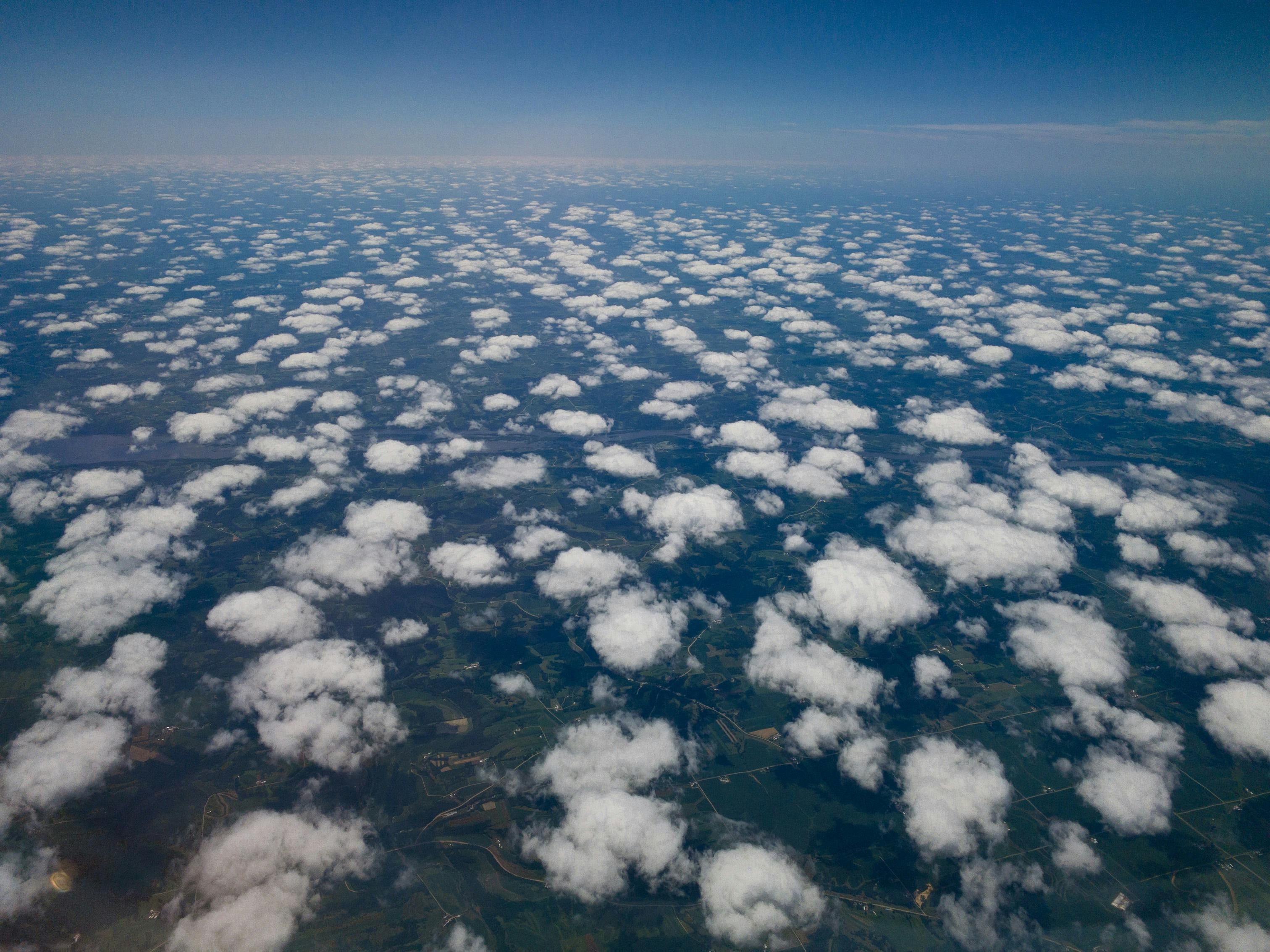 View out an airplane window of State College dotted with puffy clouds
